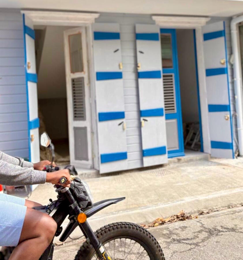 Façade colorée d’un bâtiment créole avec un scooter passant devant sur une rue ensoleillée.